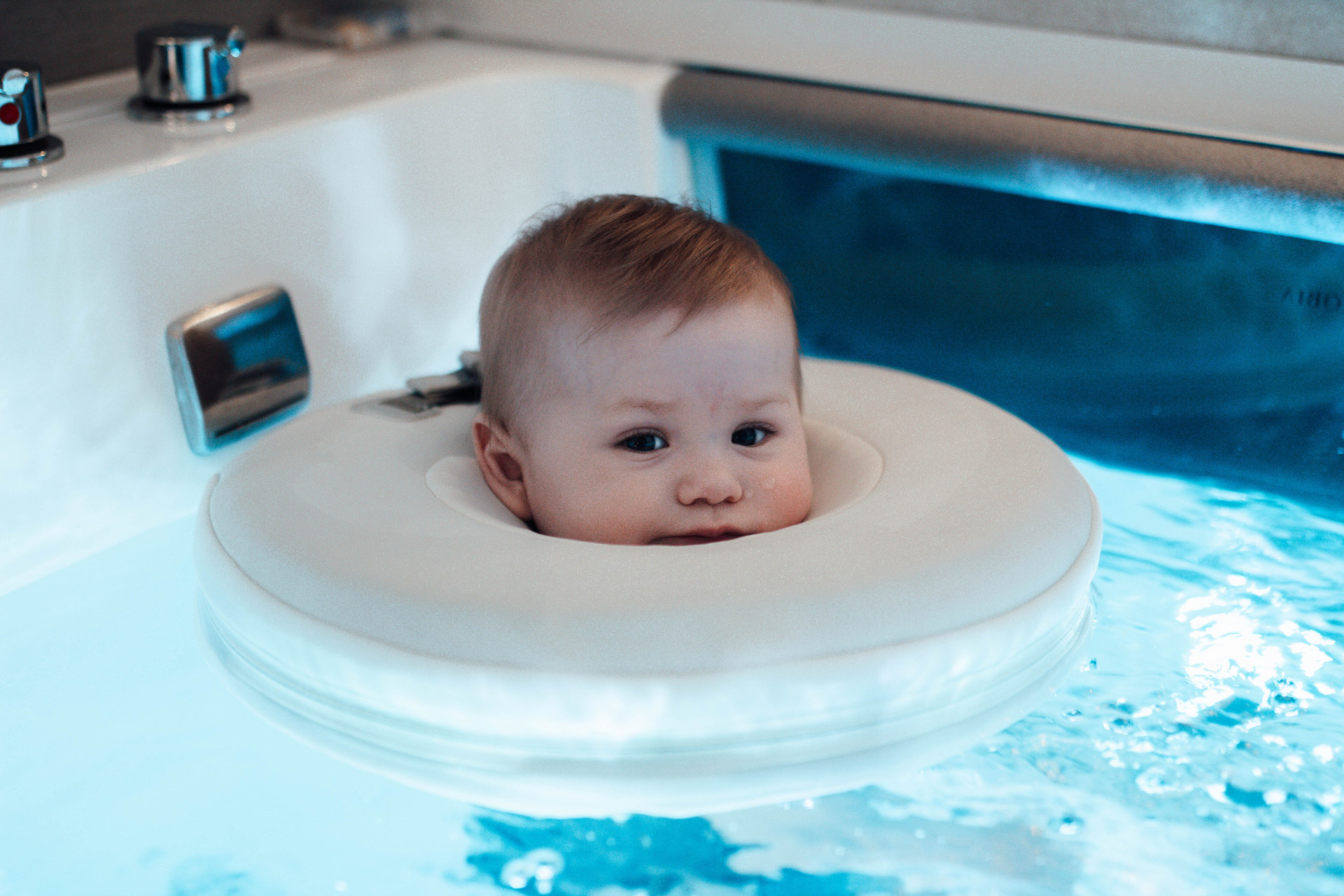 Ein Baby schaut entspannt aus seinem Schwimmring im türkisblauen Wasser des Floating-Beckens